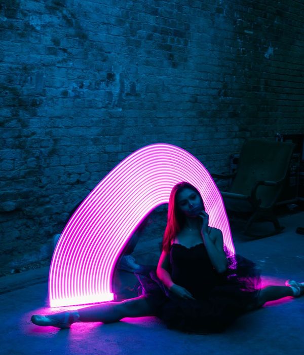 A woman performing dynamic movements in a neon lit studio.